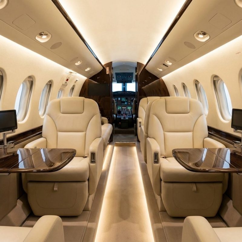 Executive luxury private jet cabin with cream leather seats, fold-out wood tables, aisle lighting and screens