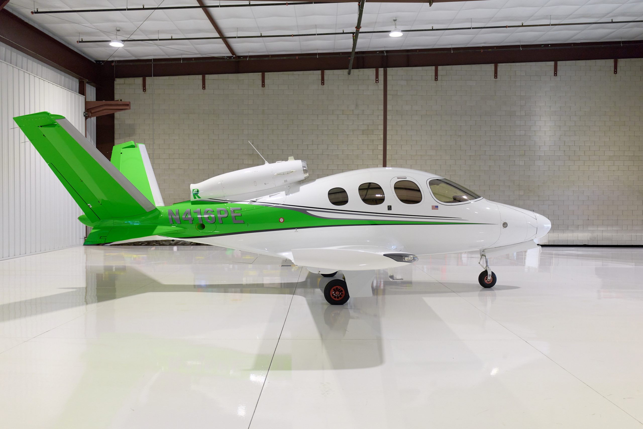 Cirrus Vision Jet SF50 in green and white livery parked in a hangar, side view, tail number N416PE
