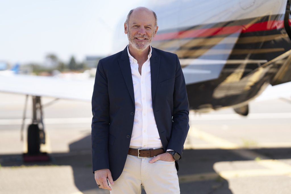 Smiling executive in blazer by private jet on airport tarmac, professional business aviation portrait